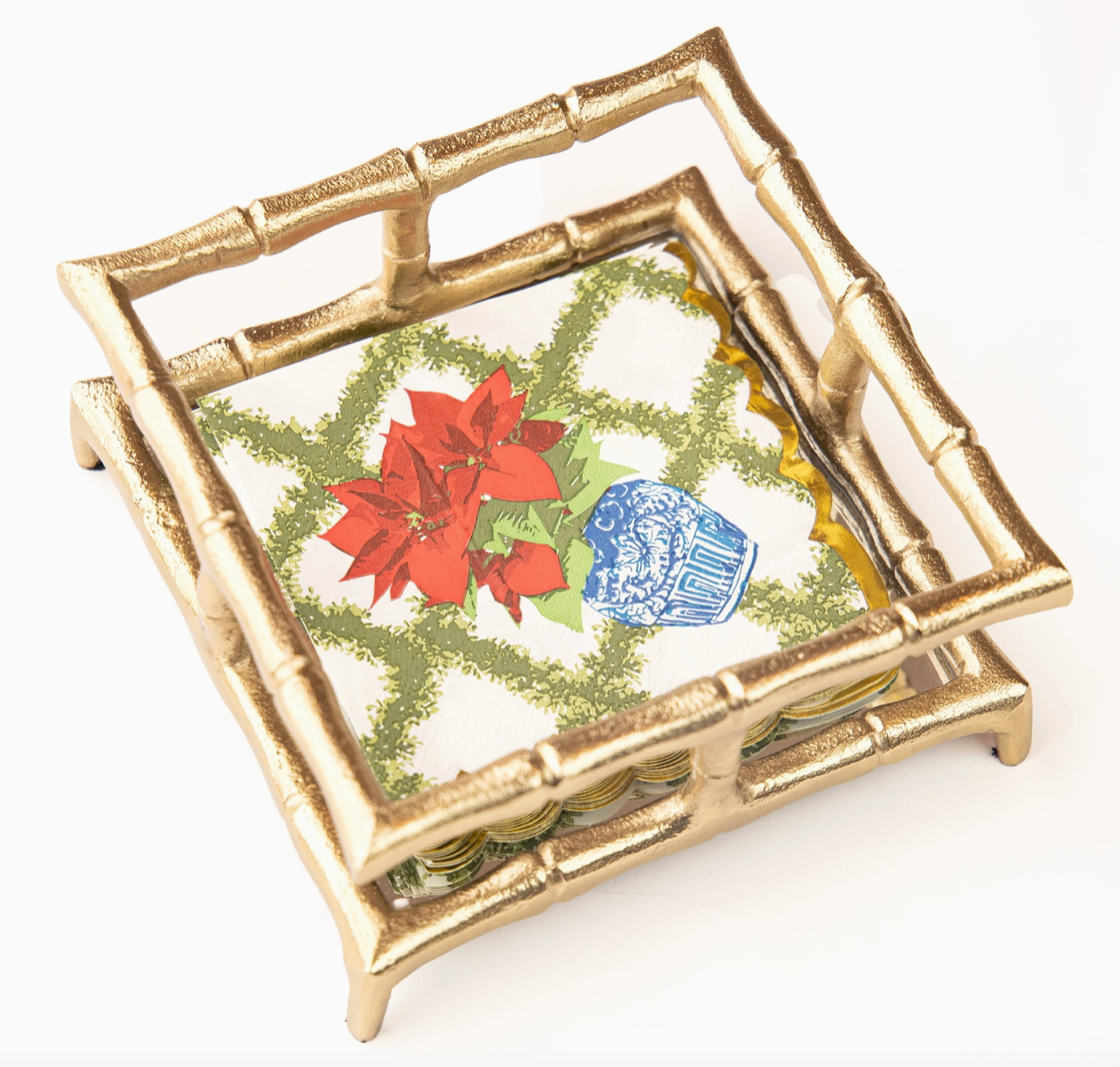 Decorative Christmas 8 Oak Lane Cocktail napkins with red poinsettias , a  green trellis. pattern and a blue vase on a white background with gold leaf effect scallop edge sitting in a gold bamboo napkin holder on a white background