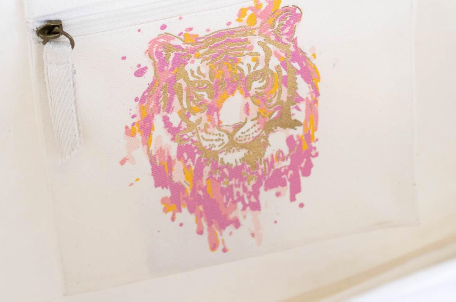 The Royal Standard brand close up of the pink orange and gold abstract tiger face with zipper tab on the side of the off white canvas tote