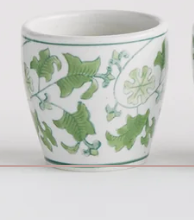 A white Napa Home and garden Brand ceramic cup decorated with a green vine and leaf pattern, shown against a plain white background.