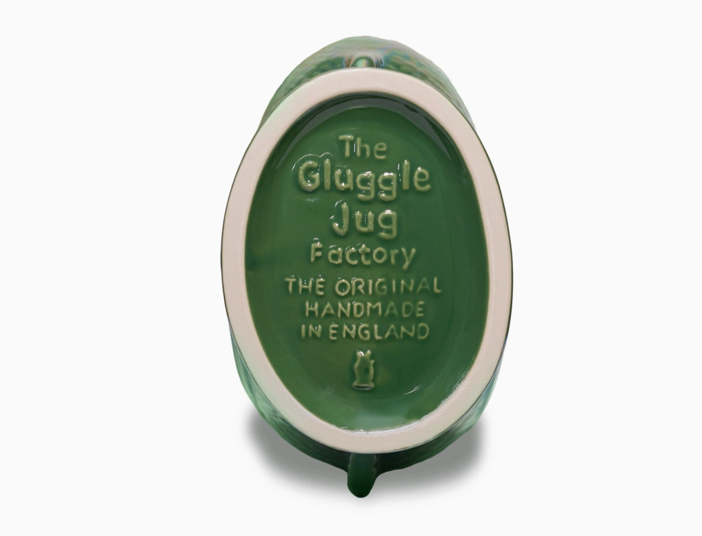 The bottom of a Gluggle jug actory brand green glazed ceramic pitcher showing embossed text that reads 'The Glaggle Jug Factory THE ORIGINAL HANDMADE IN ENGLAND' on a white background.