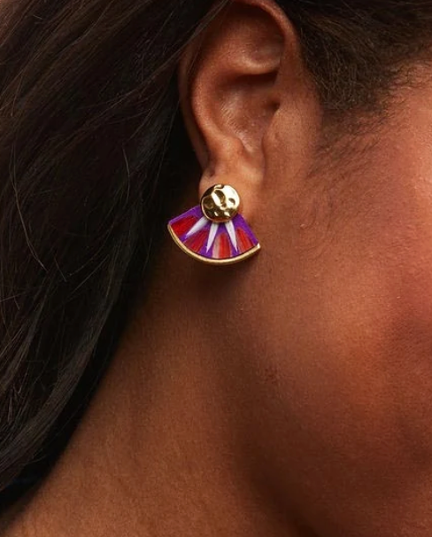 A close-up of a person's ear wearing a gold stud earring with a fan-shaped drop in orange, purple, and white feathers.