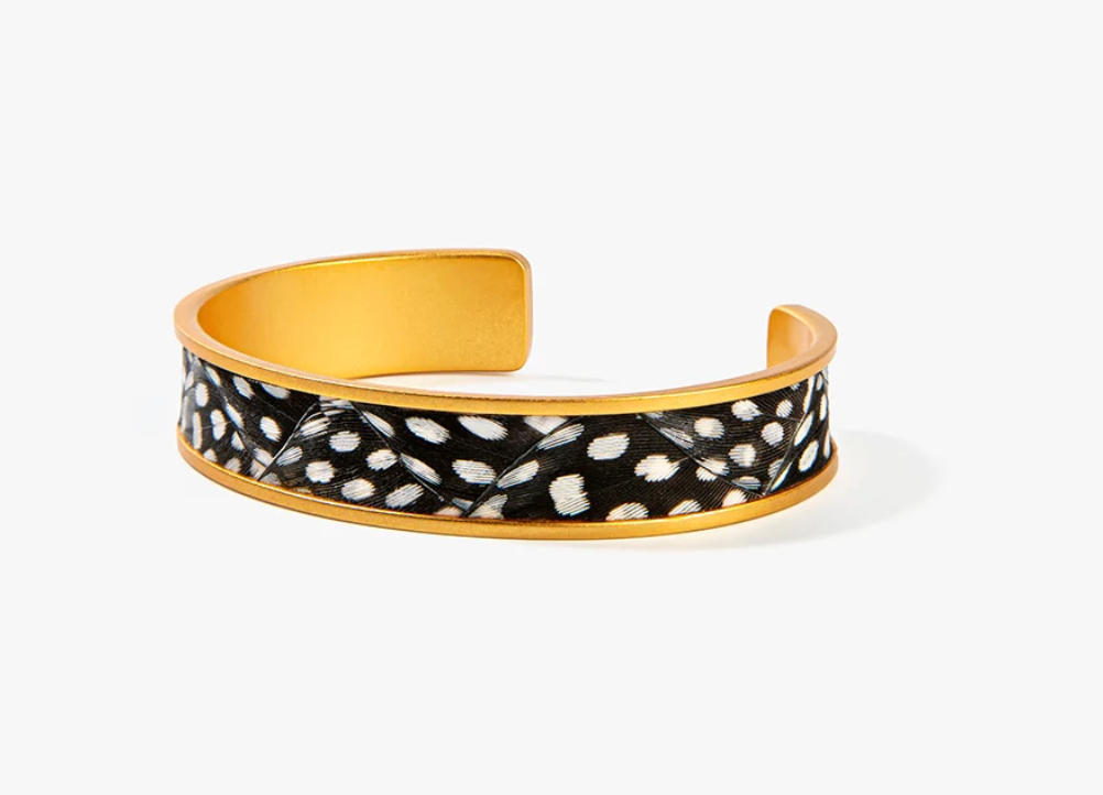 A BRACKISH BRAND gold-toned open cuff bracelet featuring black and white feathers set in gold outer band with a photographed on a clean white background.