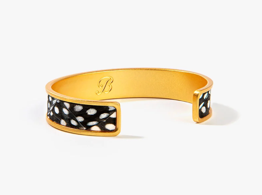 A gold-toned open cuff bracelet featuring black and white feathers set in gold outer band with a photographed on a clean white background.
