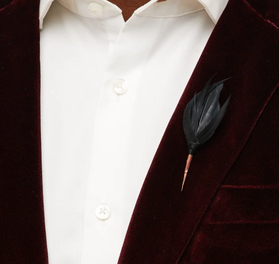 Brackish lapel pin of black feathers on a dark red suit lapel with white shirt