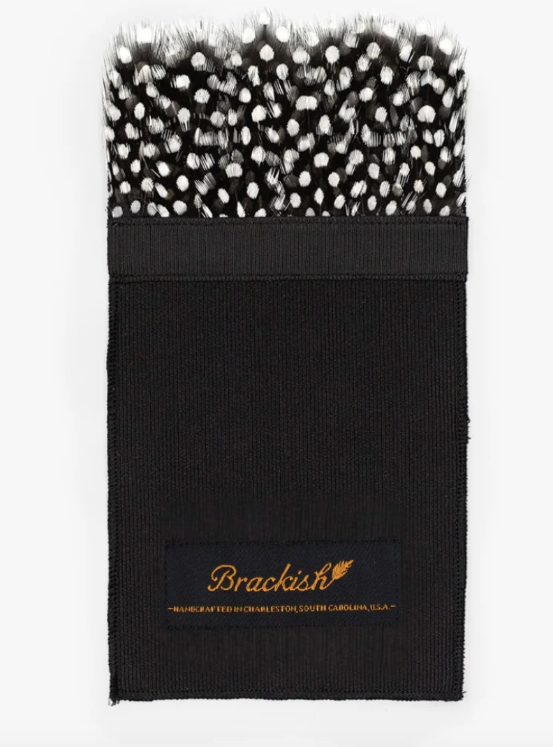 black and white guinea feather pocket square on black fabric with brackish written in gold on white background