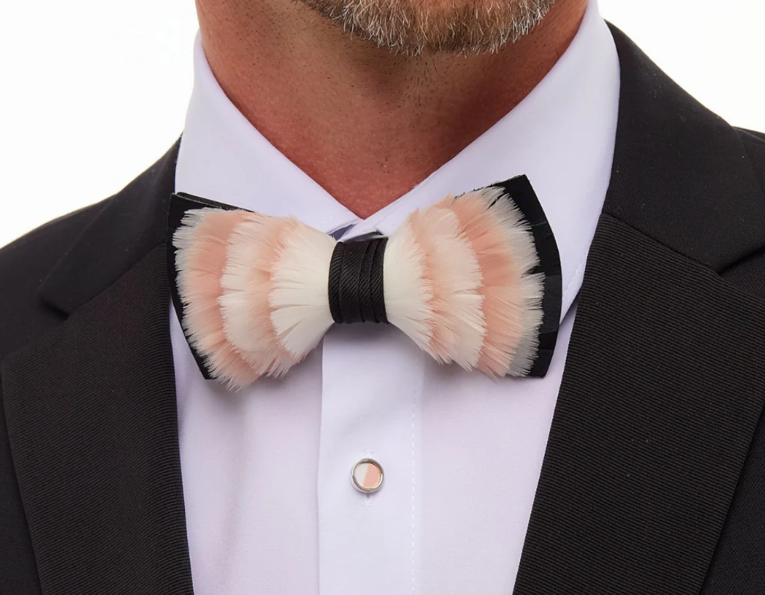 Pink white and black feather bow tie on white shirt and black coat with man's neck and chin showing on white background