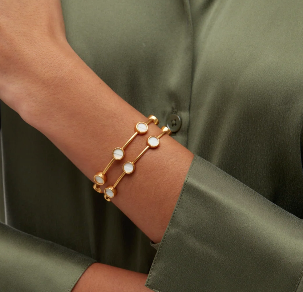 Gold cuff Brackish bracelet with round gold insets of white goose feathers on a womans arm with green satin blouse