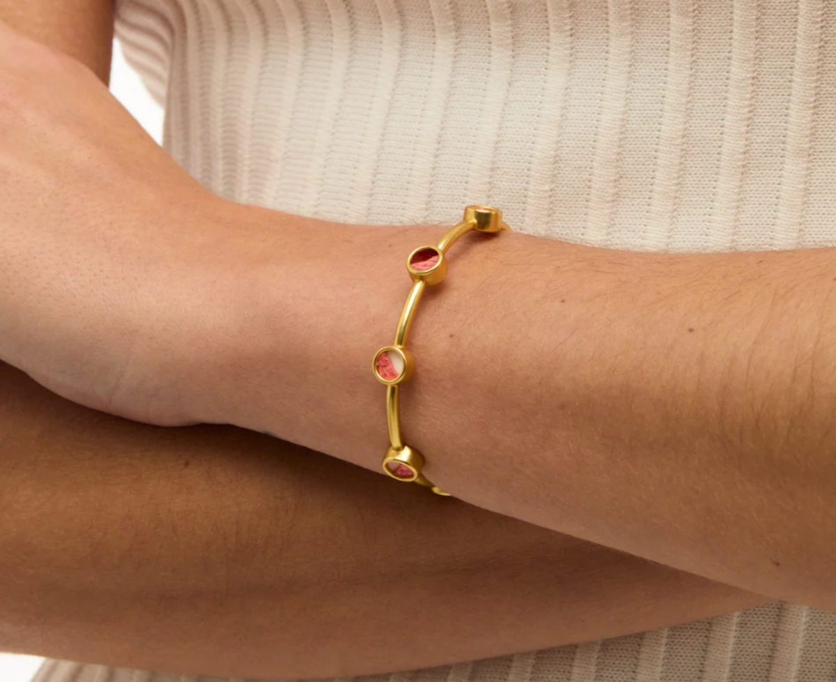 gold cuff bracelet from Brackish brand with 7 gold bezels with pink and dark feathers on womans arm with beige sweater