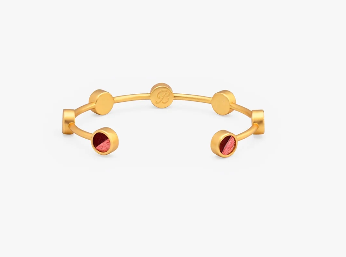 gold cuff bracelet from Brackish brand with 7 gold bezels with pink and dark feathers on white background