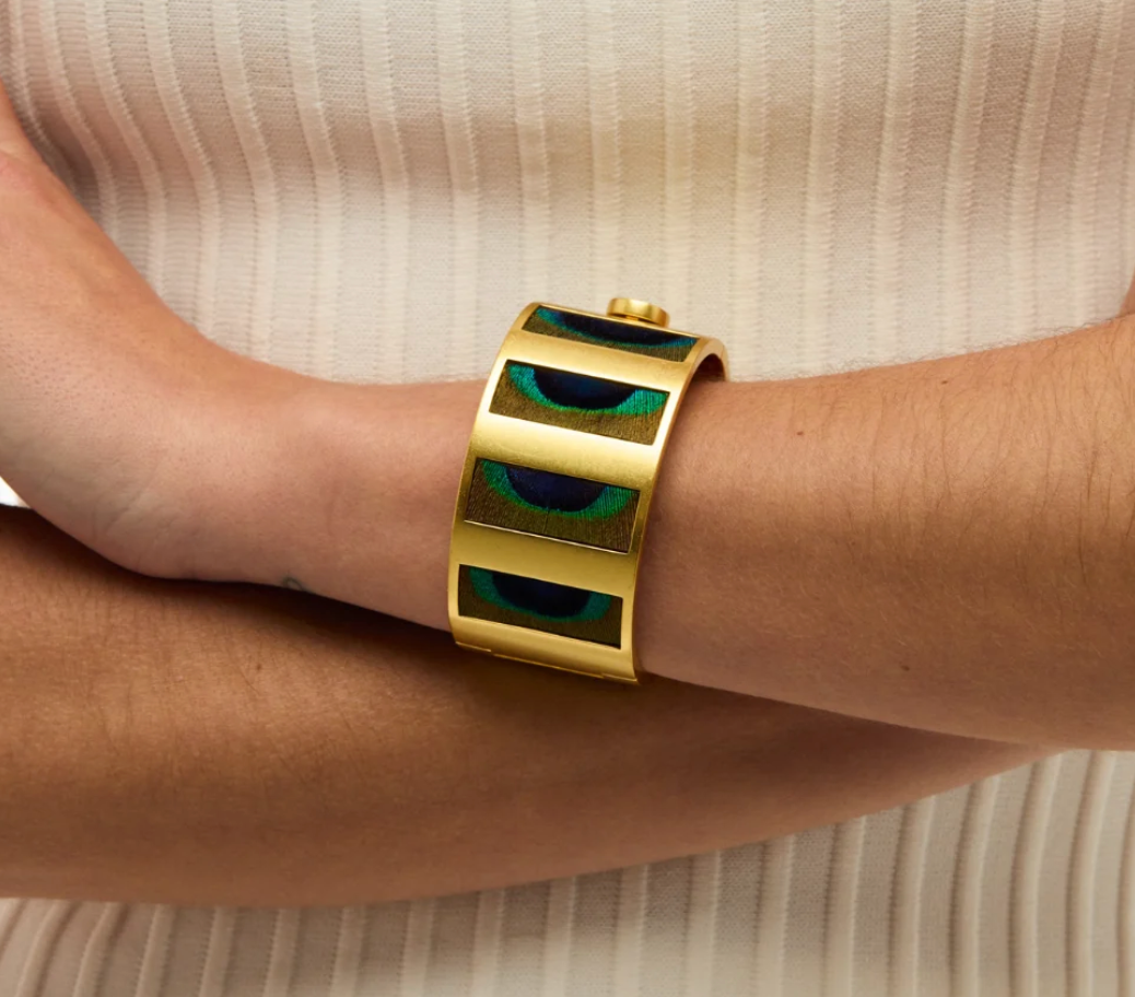 “Brackish Natalie striped peacock feather gold cuff worn on a wrist against a cream ribbed top”