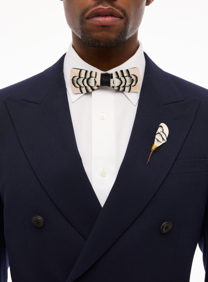 Model wearing a cream and black Brackish feather bow tie with a navy double-breasted suit and coordinating feather lapel pin.