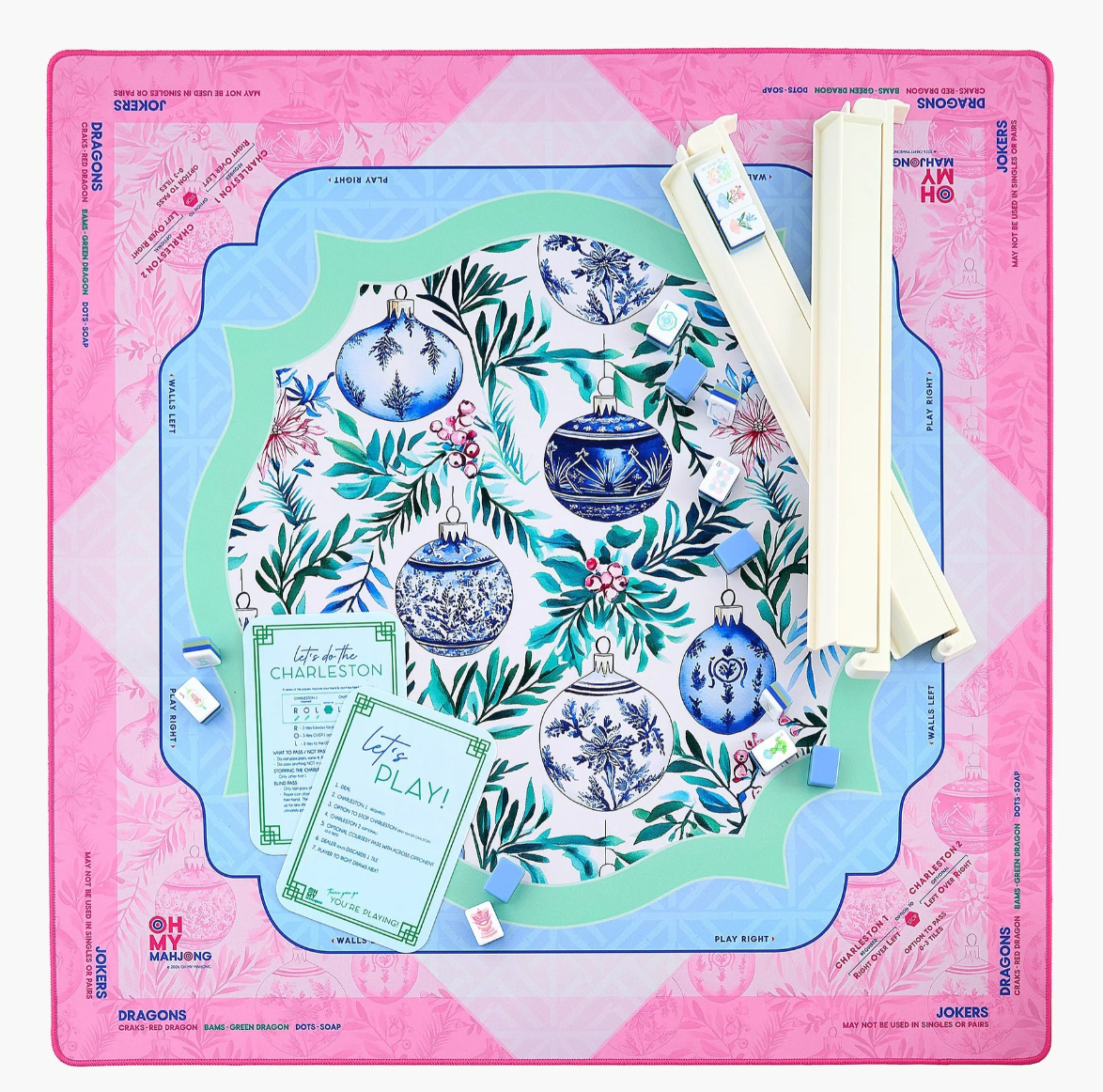 Overhead view of the Oh My Mahjong Merriment ornament-patterned mat with ivory racks, scattered tiles, and green-bordered reference cards.