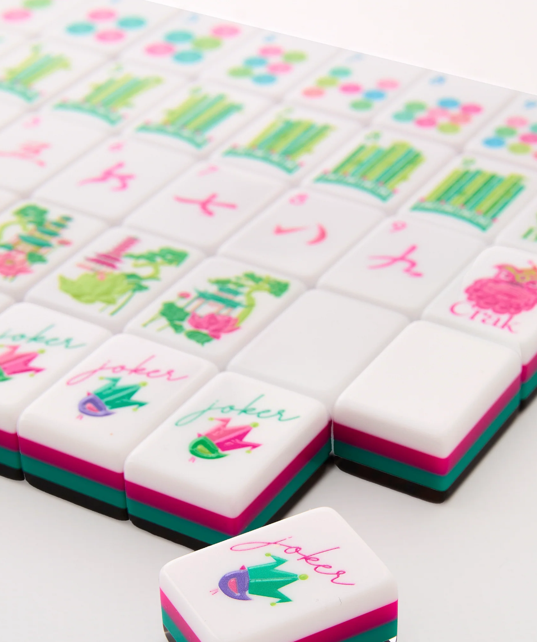 Close-up of Glow Wild mahjong tiles with pink and teal layers, illustrated suits, and jester-hat Jokers.