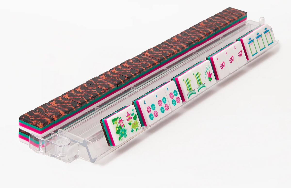 Glow Wild mahjong tiles displayed on a clear rack, showing colorful faces, layered edges, and tortoiseshell-pattern backs.