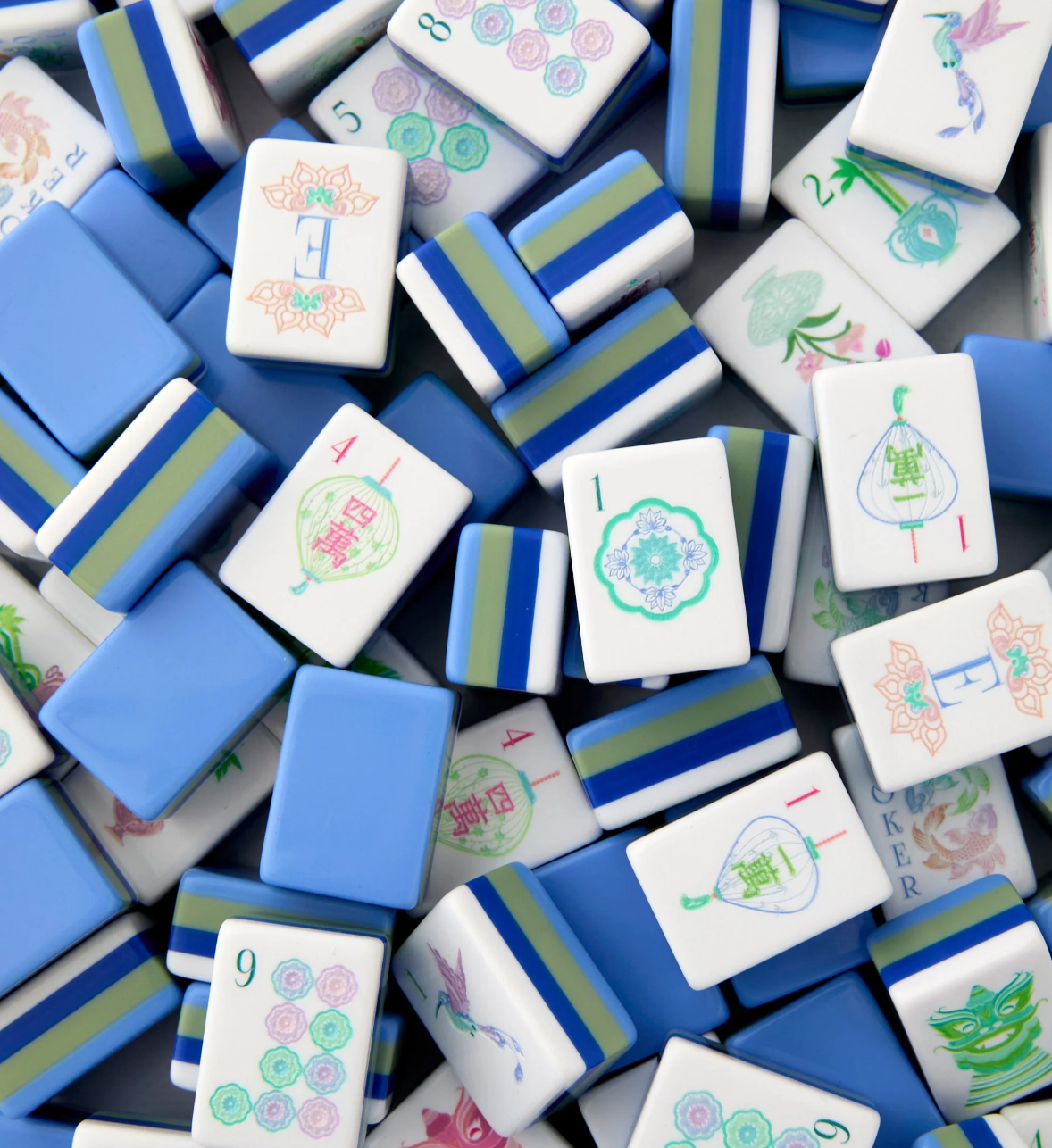 Scattered Oh My Mahjong Moonlight tiles showing blue backs, green and blue layers, and pastel lantern, bird, and dot designs.