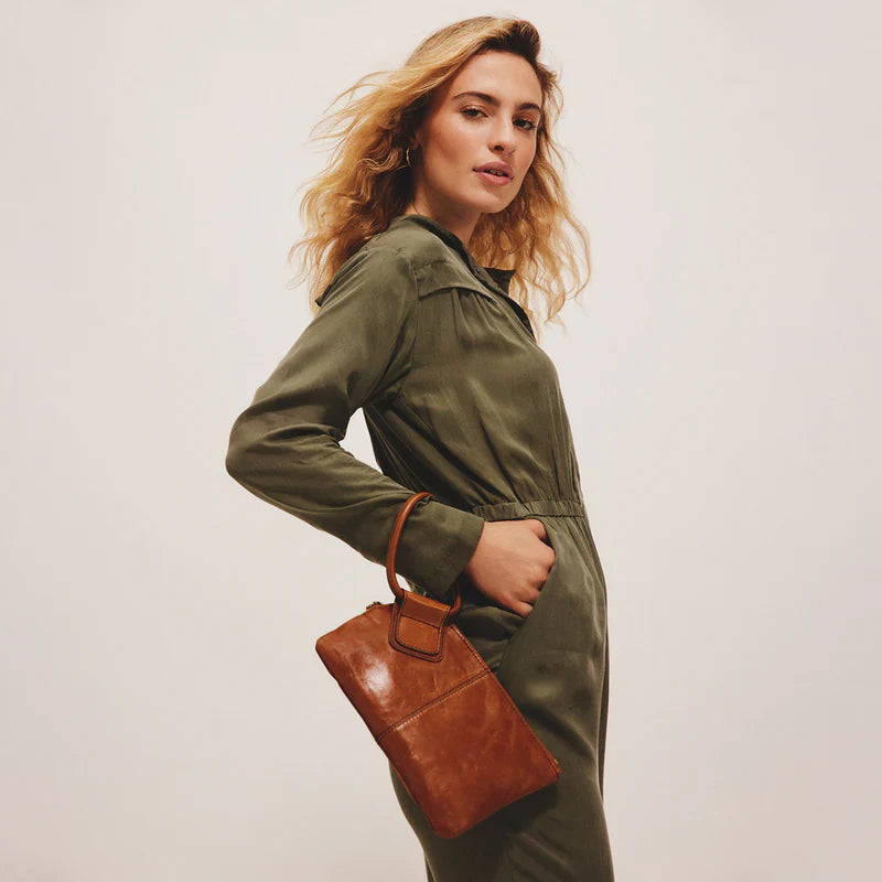 Woman wearing a green jacket holding a brown leather bag against a plain background