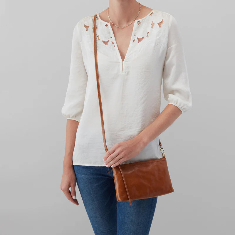 Person wearing a white blouse with cut-out details and holding a brown leather bag on a gray background