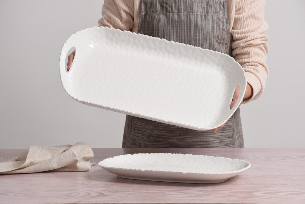 Person holding a white ceramic tray with textured edges on a wooden surface.