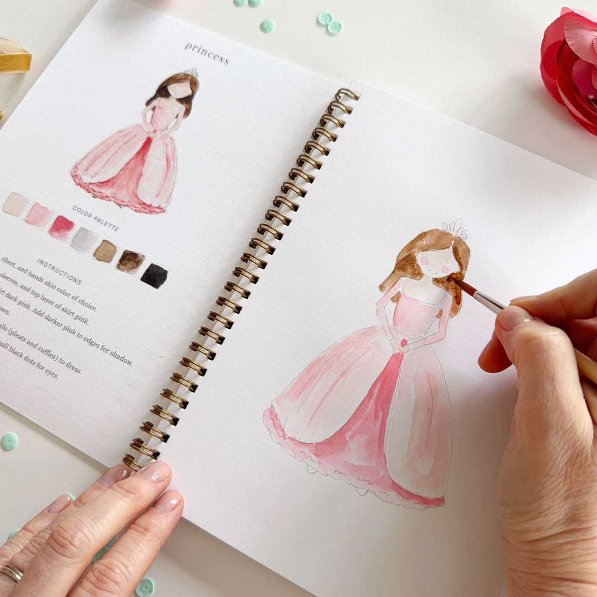 Person painting a princess in a pink dress in a sketchbook with color swatches.