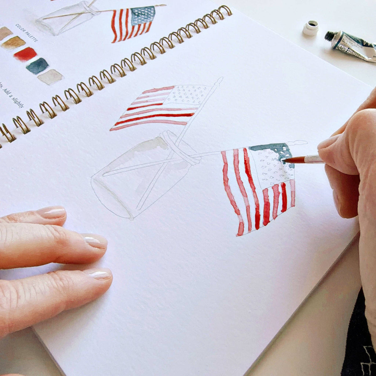 Person painting American flags in a notebook with a paintbrush.