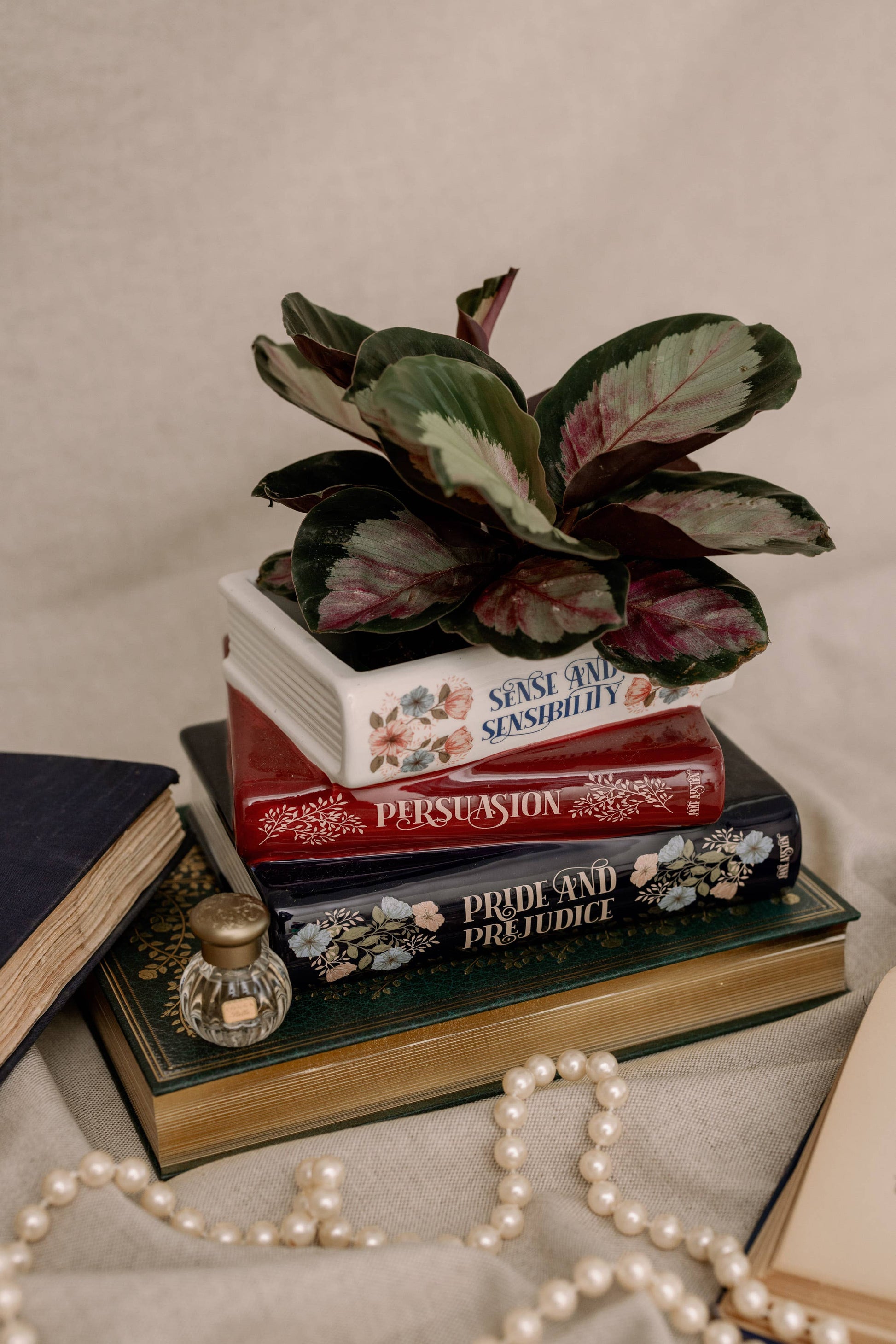 Steel Mill brand 3 stack book decorative vase/planter with Jane Austen titles on each one, with a potted plant on top, pearl necklace in foreground