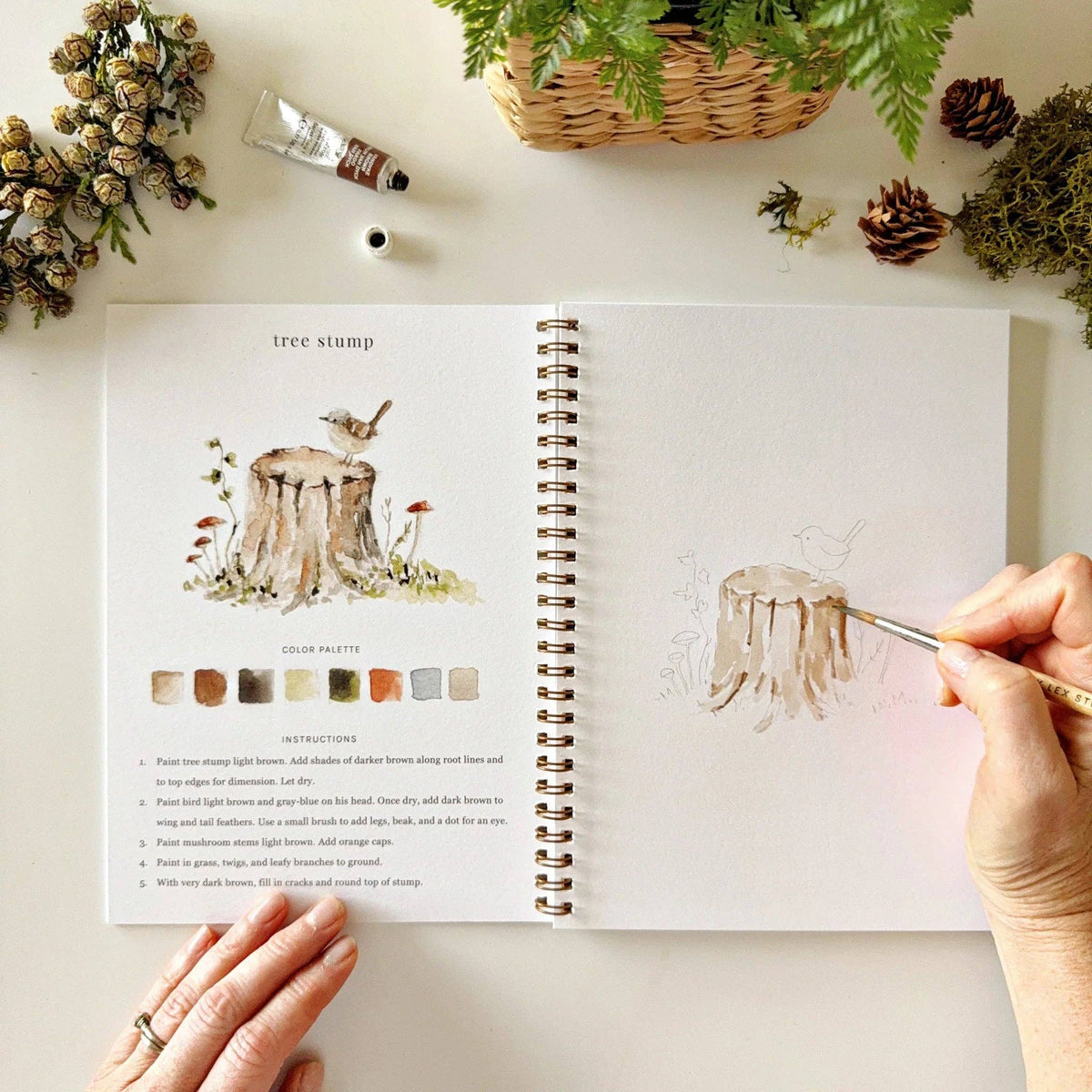 Person painting a tree stump illustration from a book with nature-themed decor.