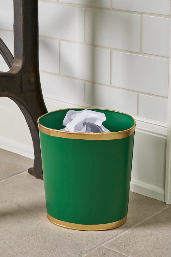 Green trash bin with gold rim on a tiled floor against a white tiled wall.