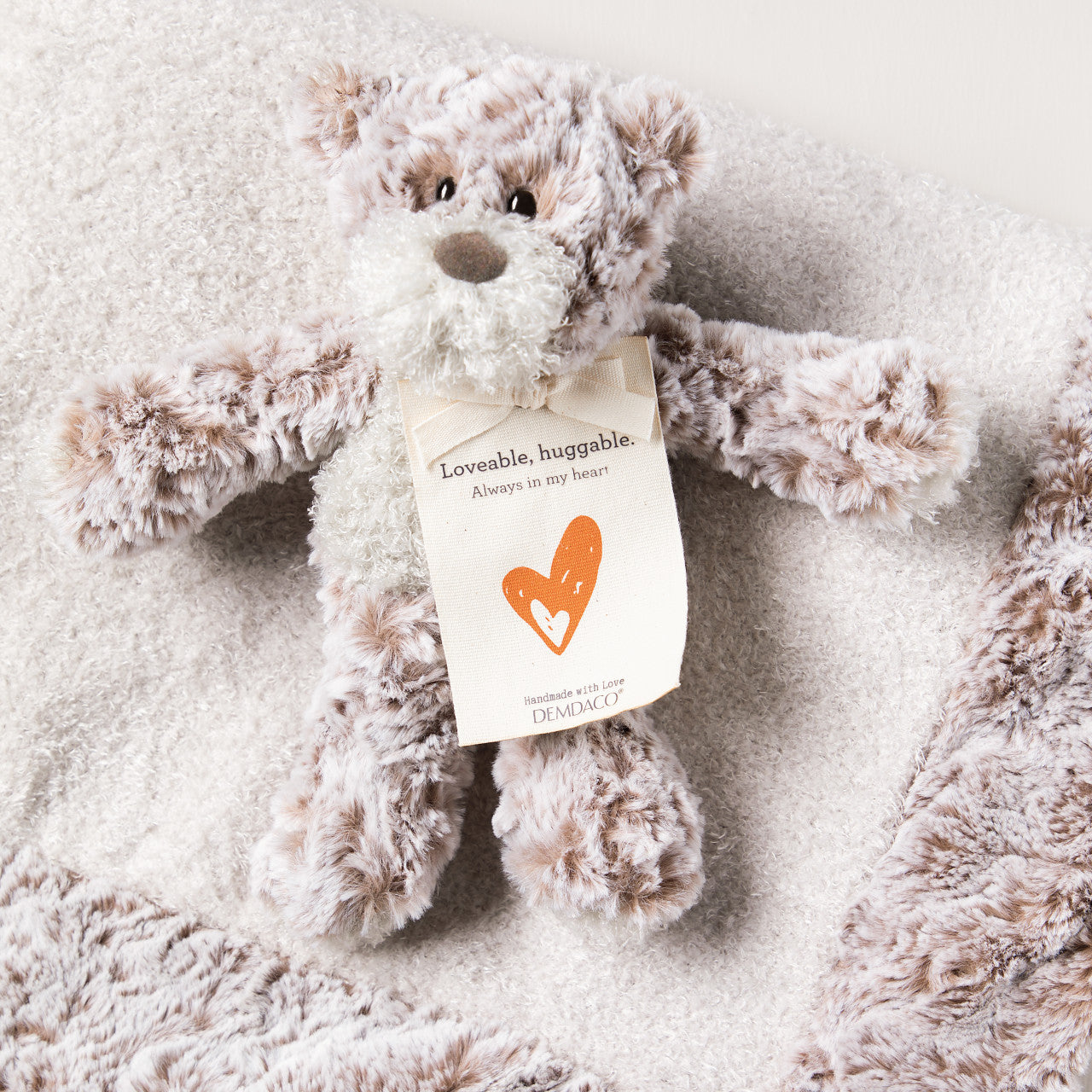 Plush teddy bear with a tag on a soft, textured surface