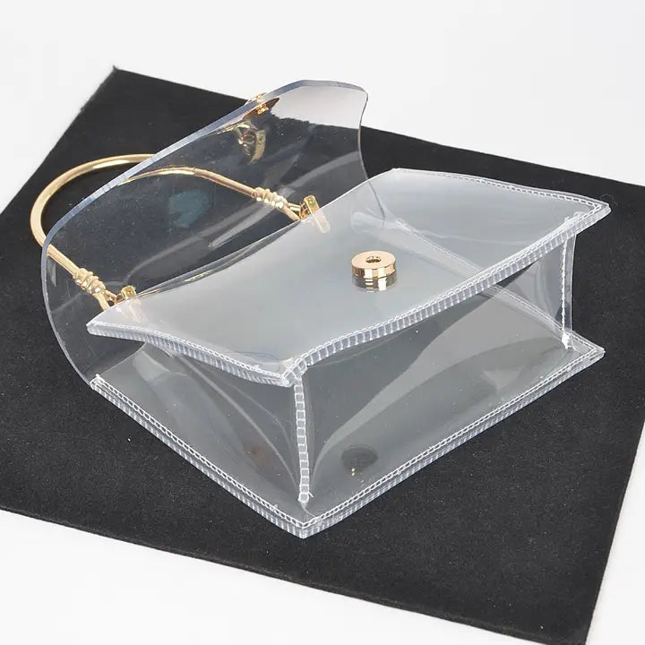 Transparent clear flap clutch with gold metal handle and gold ball button closure, open flap view from above on black velvet showing interior capacity
