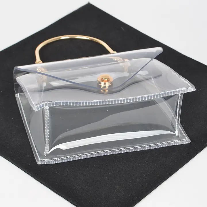 Transparent clear flap clutch with gold metal handle, open flap angled view on black velvet showing structured sides and gold button detail