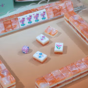 A set of mahjong tiles arranged in a game-like layout on a beige surface, with a small purple die nearby.