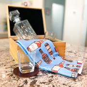 Tea Towel - Bourbon - Microfiber- picture is of a blue tea towel with bottles of bourbon on it and a whiskey glass with a Decanter in a brown wooden box  sitting on a granite counter top