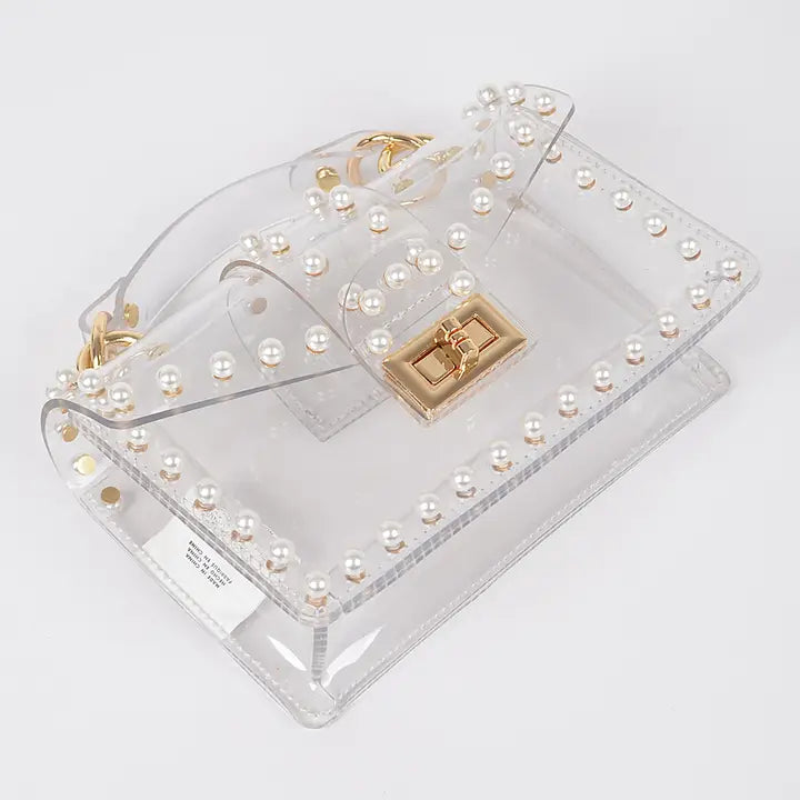 Transparent pearl-studded clear clutch bag laid flat showing gold twist lock closure and faux pearl border detail, top-down angle view