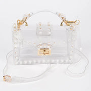 Transparent clear clutch bag with faux pearl embellishments and gold twist lock closure, front view with single top handle and removable crossbody strap on white background