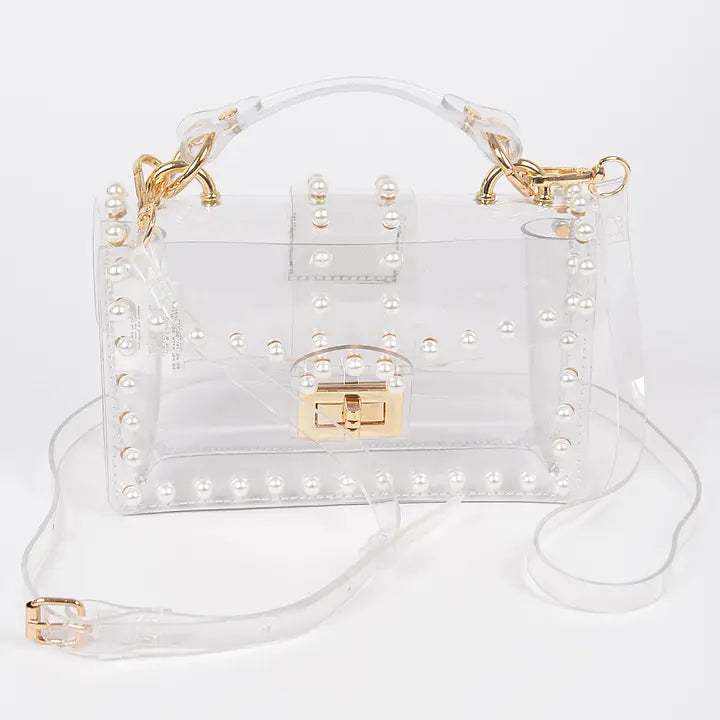 Transparent clear clutch bag with faux pearl embellishments and gold twist lock closure, front view with single top handle and removable crossbody strap on white background