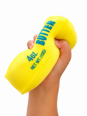 A hand squeezing a bright yellow novelty butter-shaped object with blue text reading 'BUTTER' and '4.0 OZ.