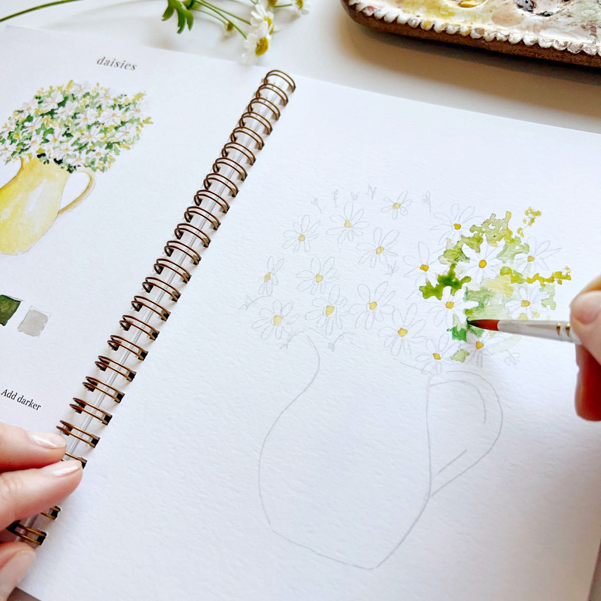 Person drawing flowers in a notebook with a paint brush