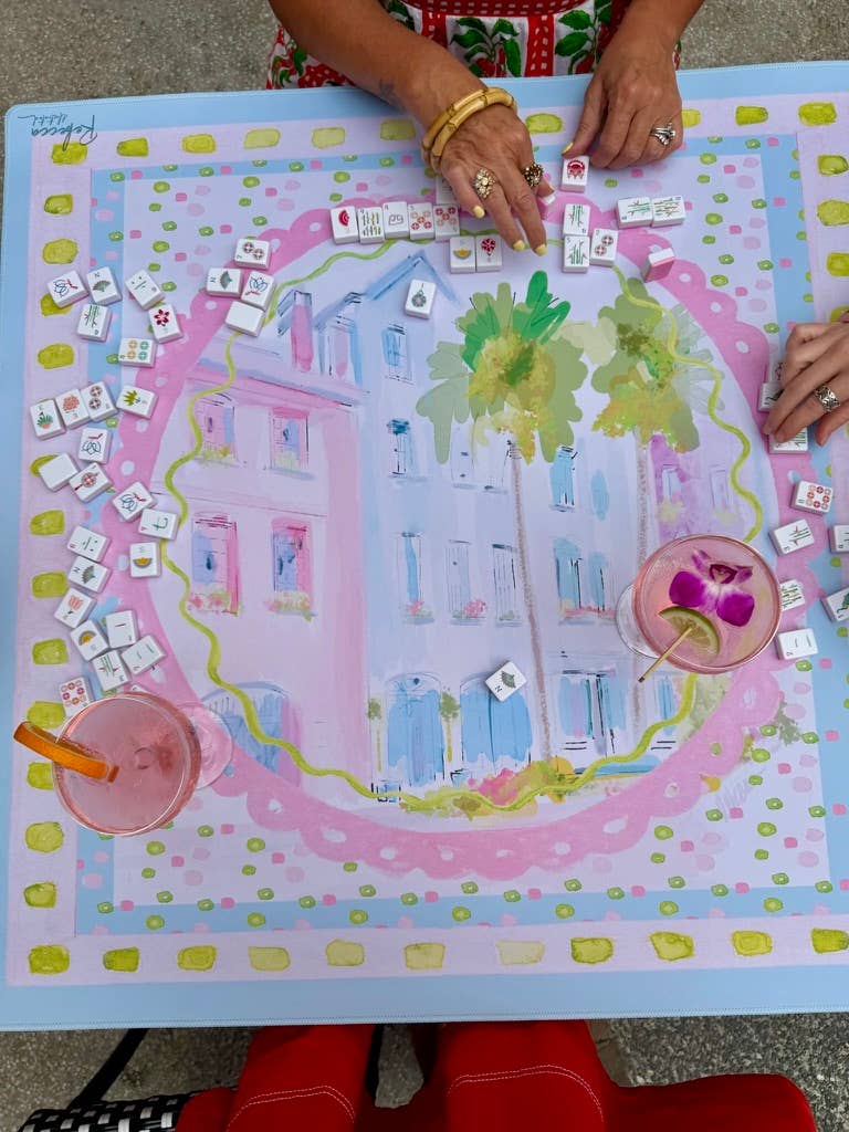 Mahjong game mat with colorful design and hands playing on a pink and blue themed board