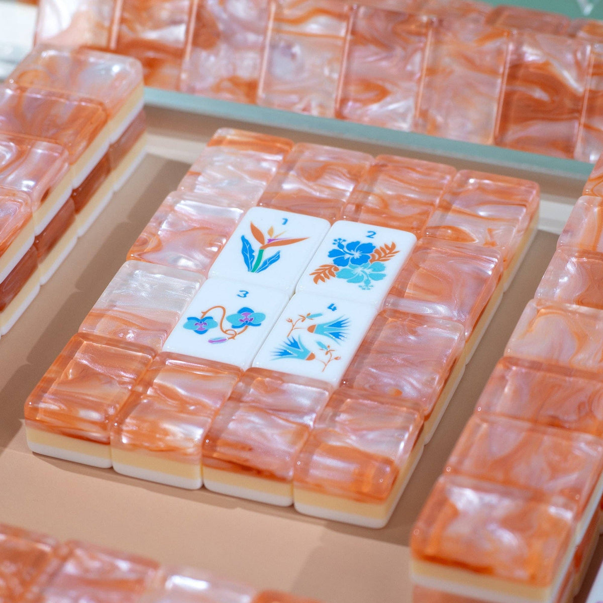 A close-up of a set of translucent orange and white marbled rectangular tiles arranged in a grid, with three white tiles featuring blue and orange floral designs placed in the center.