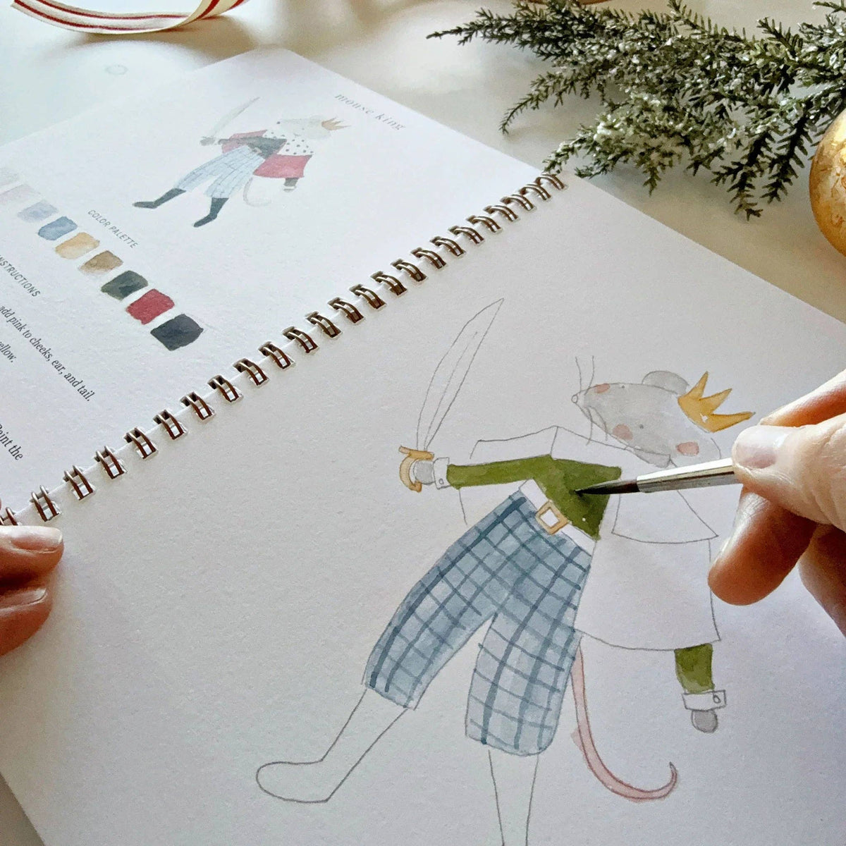 Person painting a drawing of a character in a notebook with a paintbrush