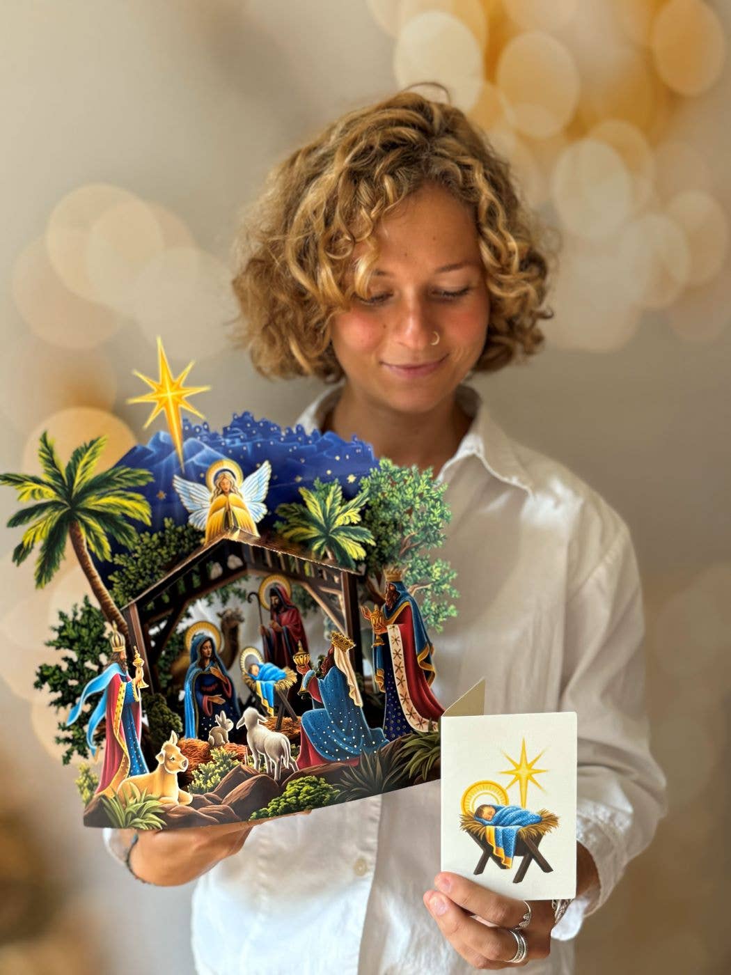 Person holding a detailed nativity scene pop-up card and a smaller card with a star and baby Jesus in a manger.