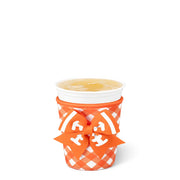 An orange and white gingham paper cup sleeve with a matching orange ribbon bow featuring white lettering, holding a white styrofoam cup with a yellow drink on a white background.