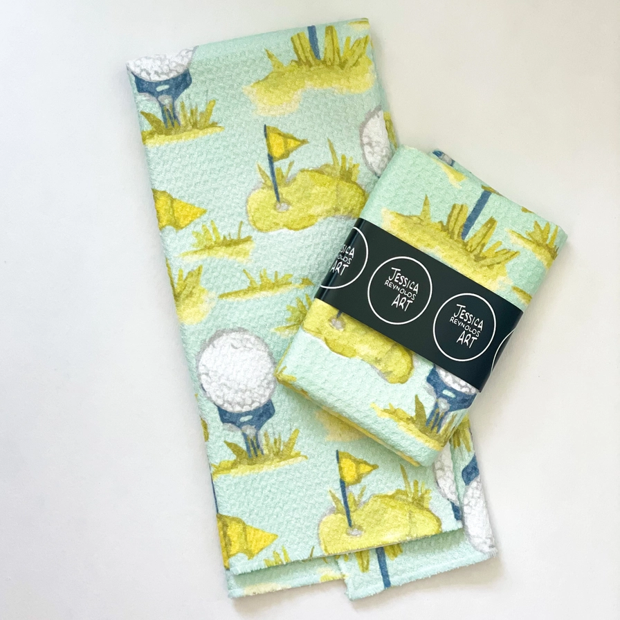 Tea Towel - Golf - Microfiber- picture is of two of the golf tea towels with golf holes and golf balls on tees, one of the tea towels is wrapped and says Jessica Reynolds Arron a white background