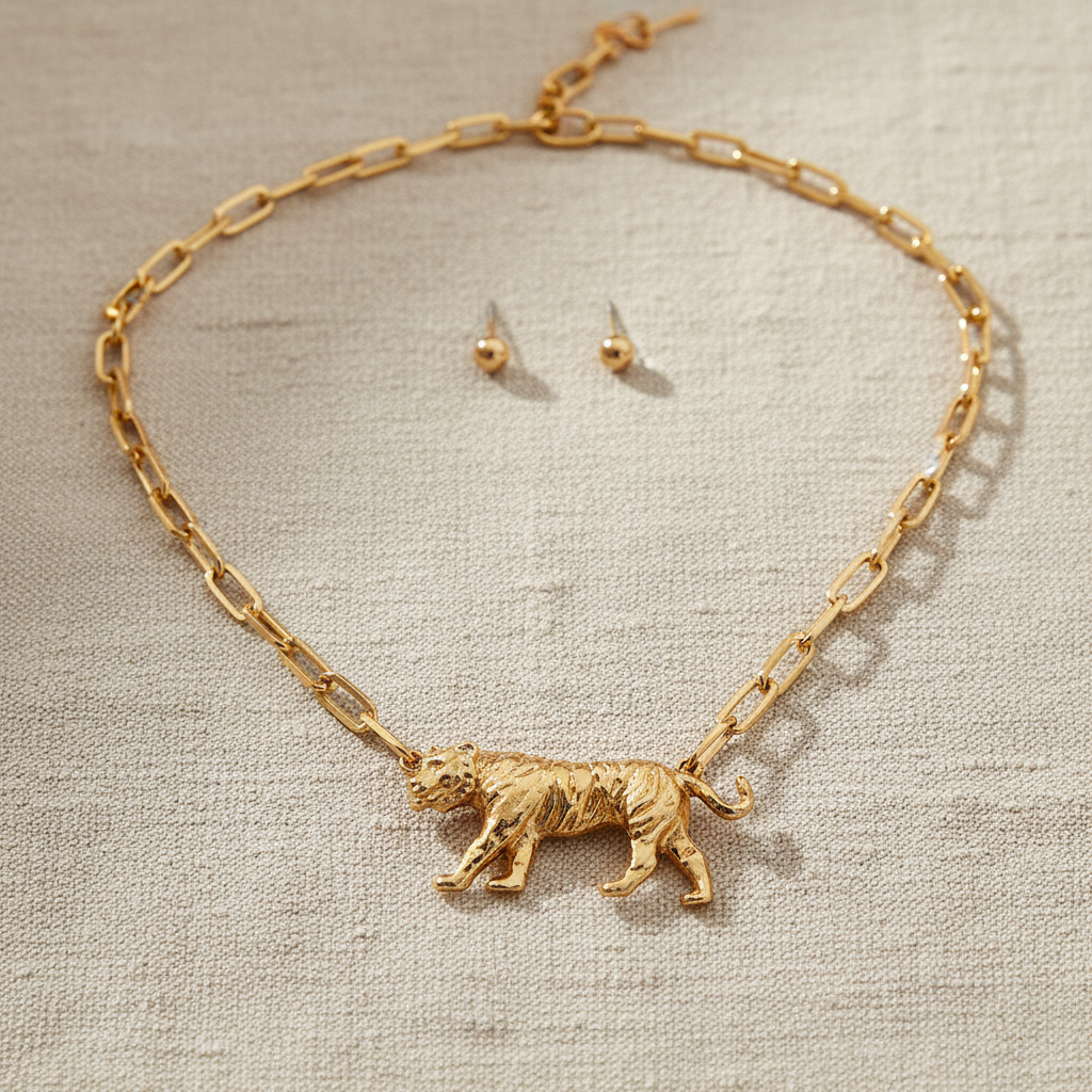 Grace Ann Designs Gold necklace with tiger pendant and matching earrings on a textured surface