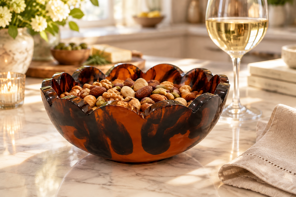 Laura Park tortoise shell scalloped edge resin snack bowl filled with mixed nuts on a marble kitchen counter with a glass of white wine and linen napkin