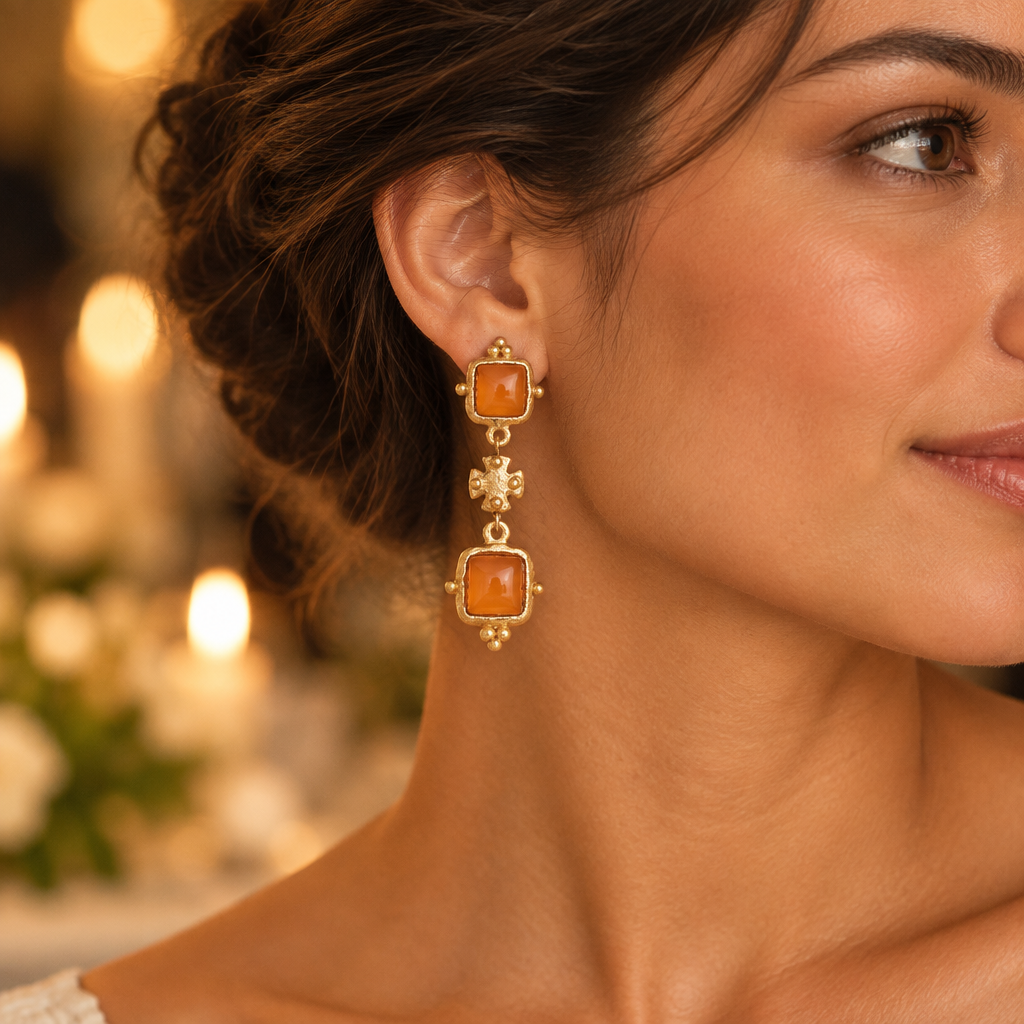 Orange French glass tier earring with Maltese Cross bead and handcast gold finish worn at a softly lit dinner setting