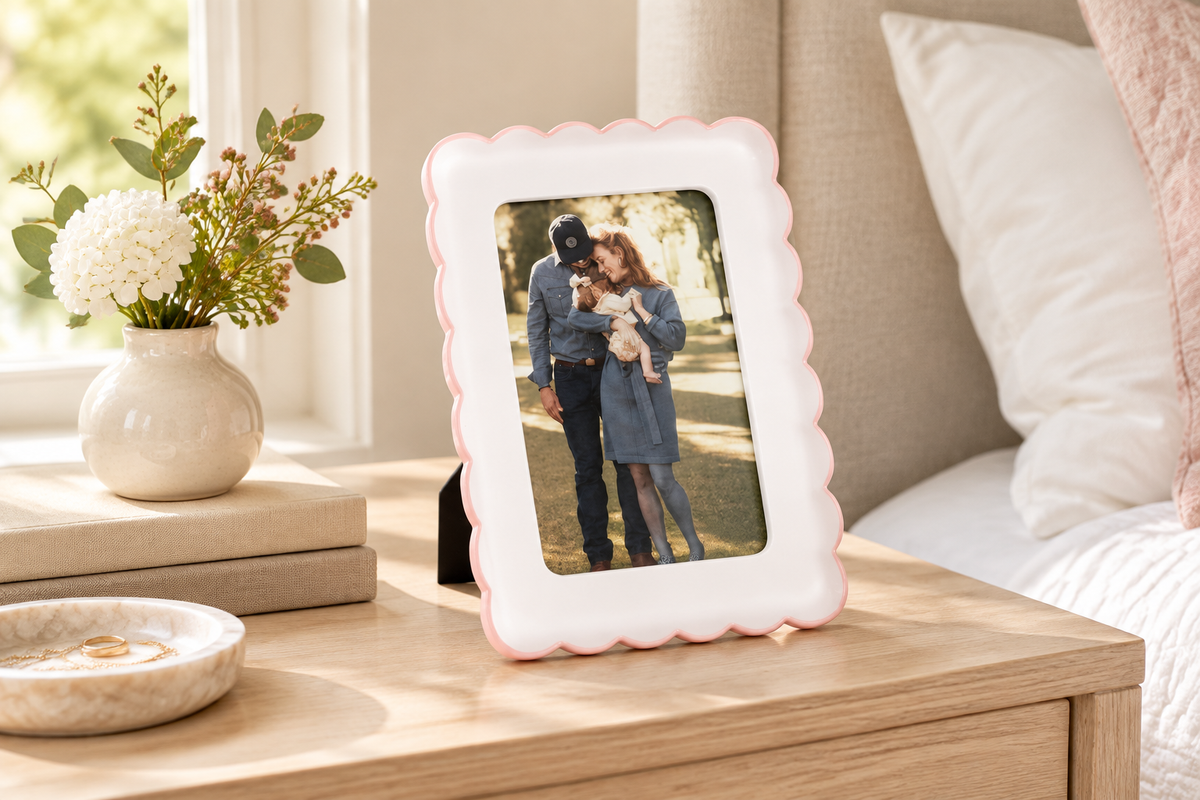 Pink scalloped resin picture frame holding a 4 x 6 photo on a softly styled bedroom nightstand