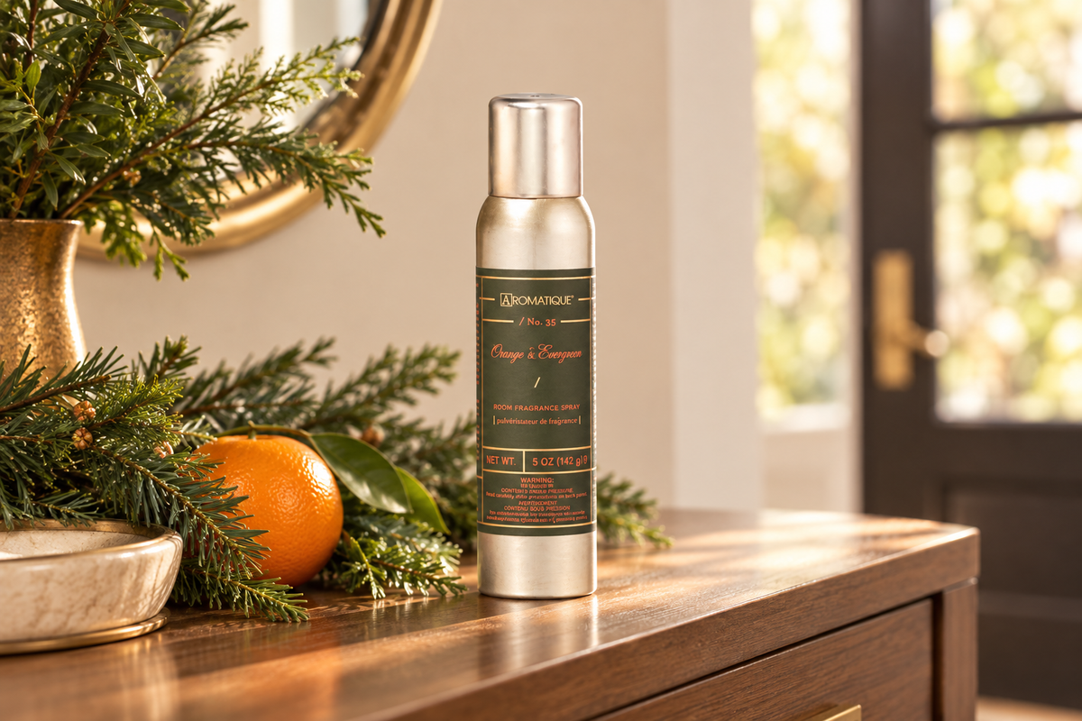 Aromatique Orange and Evergreen 5 oz room spray on an entryway console with evergreen branches and an orange