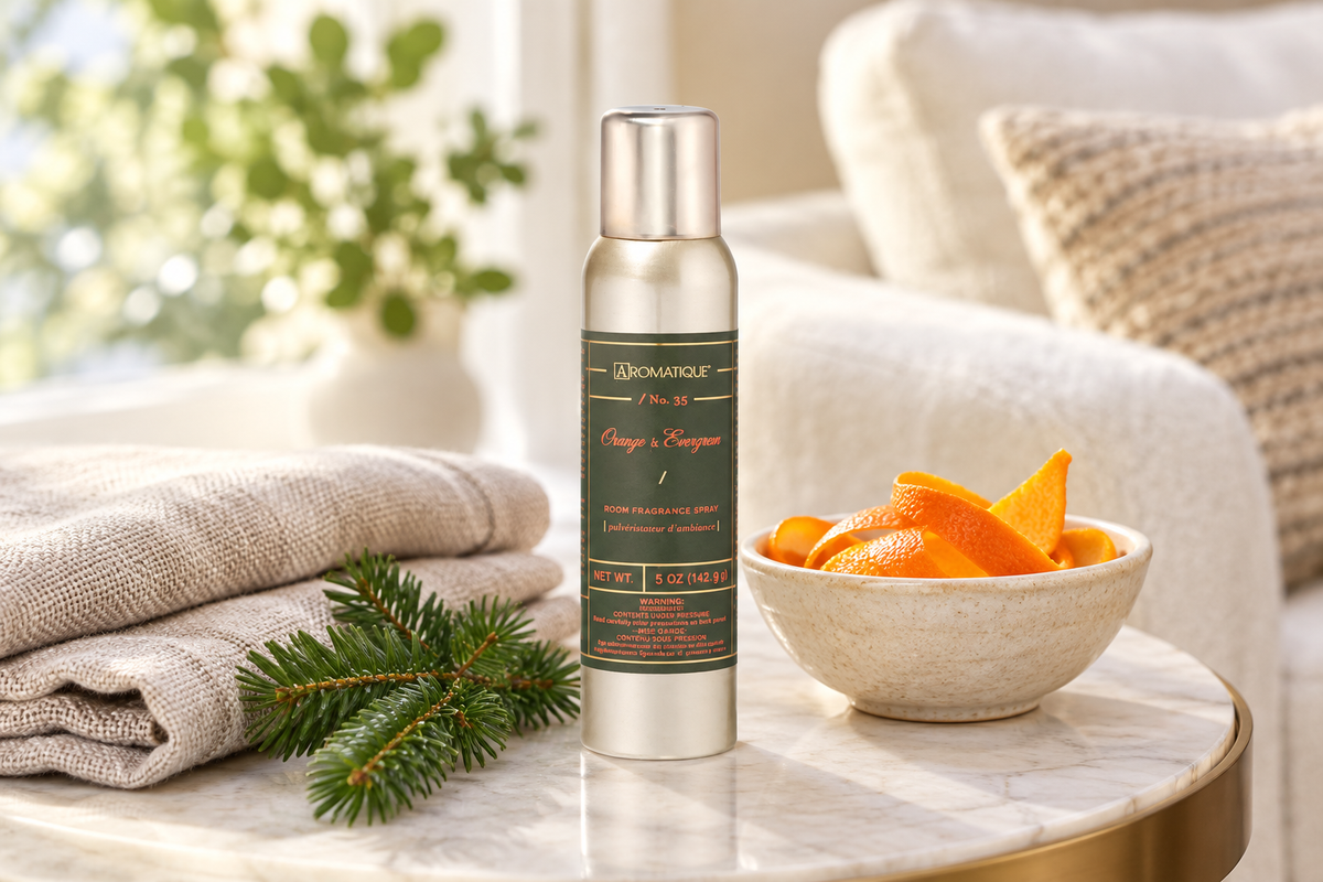 Aromatique Orange and Evergreen 5 oz room spray on a living room side table with linen, evergreen, and orange peel