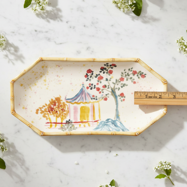 Decorative plate with artistic design on a marble surface with flowers and a ruler for scale. Hand-Painted Stoneware Decorative Plate with Palm Tree & Bamboo Design by Creative Co-Op